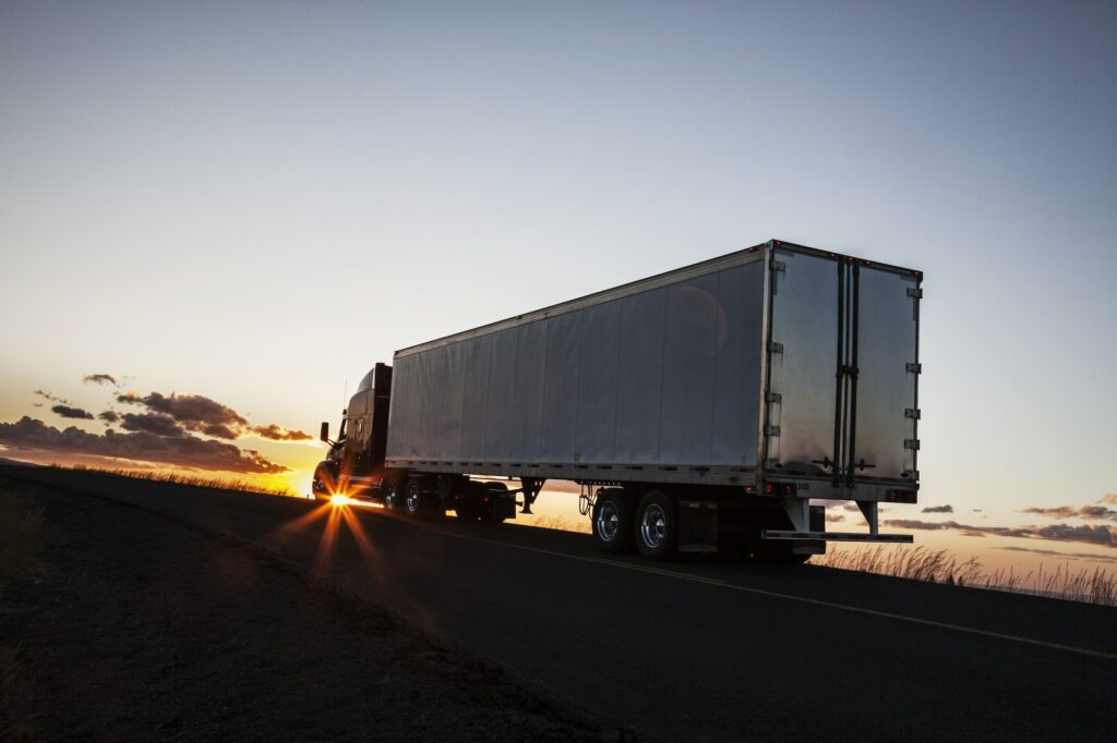 Silhouette of a commercial truck driving on a highway at sunset.